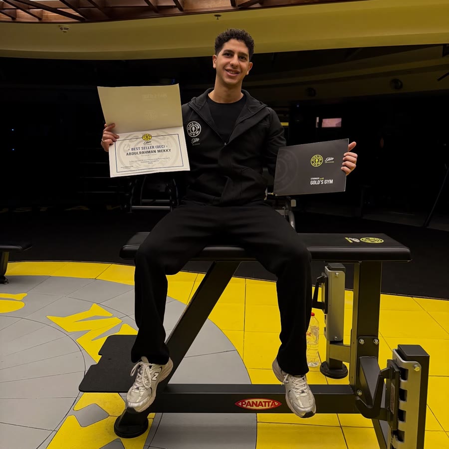 Meky sitting on a gym bench holding his Gold's Gym Elite Best Seller certificate and a Stronger with Gold's Gym folder