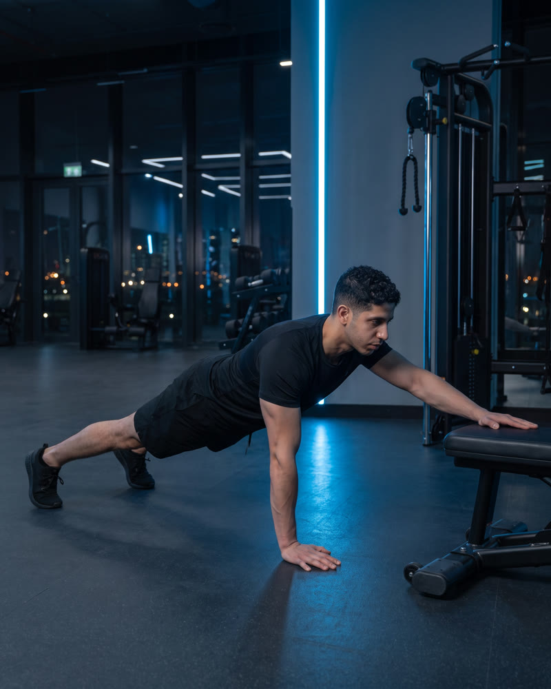 Meky in a high plank, reaching one hand forward onto a bench