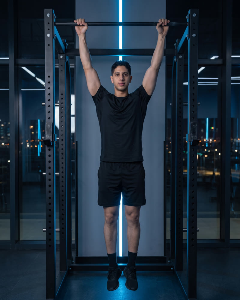 Meky hanging from a pull-up bar in a full dead hang, arms straight