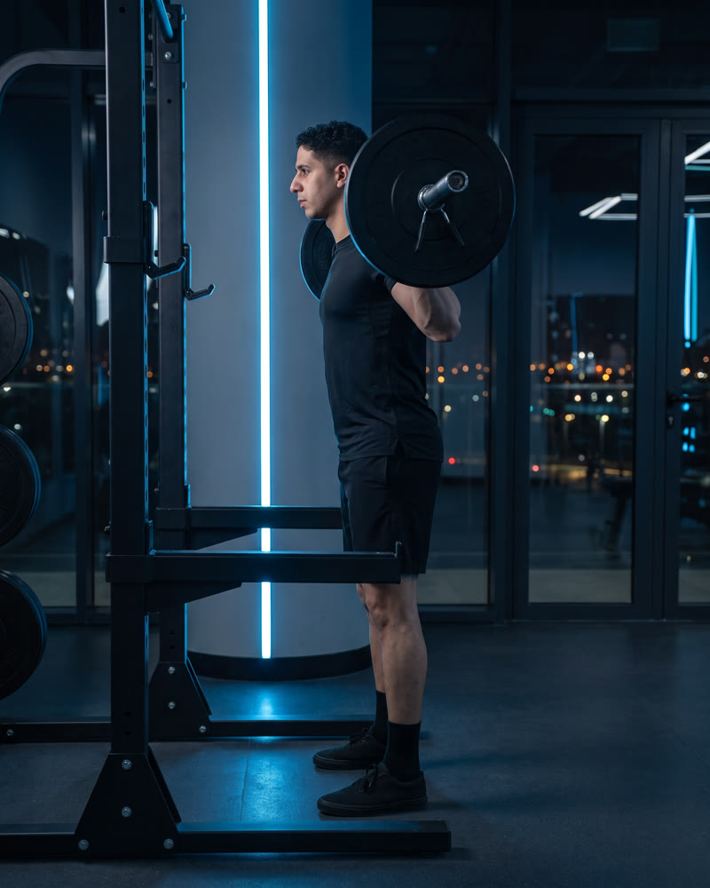 Meky standing in a squat rack with a loaded barbell across his upper back